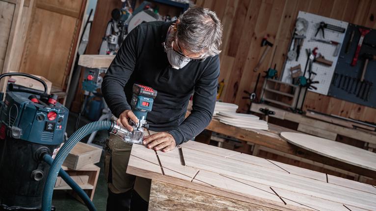 안전 장비를 착용한 사람이 전동 공구를 사용해 나무판에 홈을 파고 있습니다.