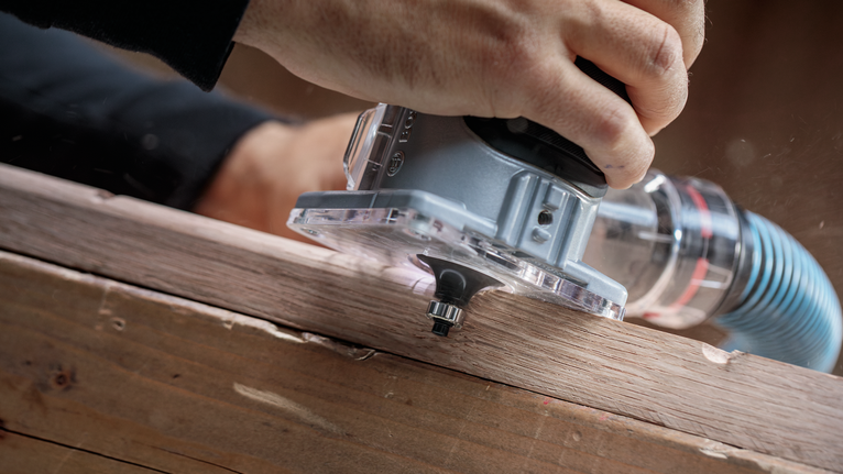 사람이 휴대용 라우터를 사용해 나무판의 가장자리 모양을 만들고 있습니다.