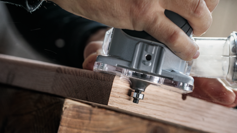 사람이 나무판 가장자리를 따라 전동 트리머를 조종하고 있습니다.