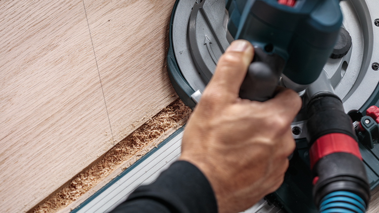 사람이 원형 톱을 조작하여 직선을 따라 나무를 자릅니다.