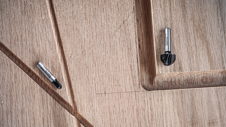두 개의 라우터 비트가 홈이 파인 조각된 나무 표면 위에 놓여 있습니다.