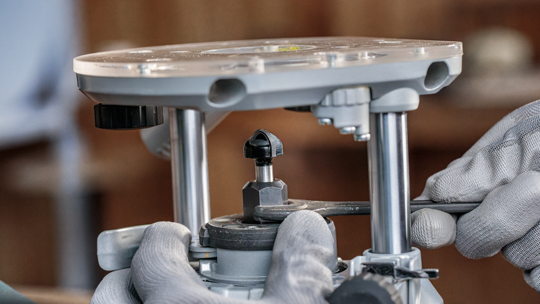 안전 장비를 착용한 사람이 렌치를 사용하여 라우터 도구를 조정하고 있습니다.