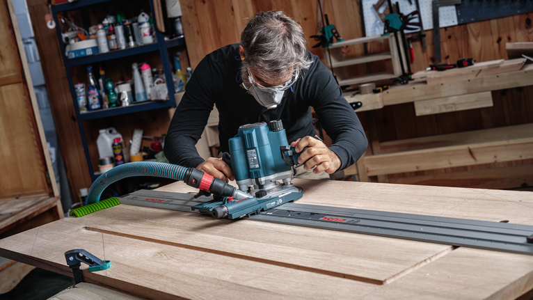 안전 장비를 착용한 사람이 라우터를 트랙을 따라 움직여 나무판을 만듭니다.