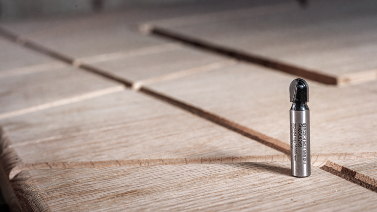 홈이 있는 나무 표면 위에 똑바로 세워진 금속 라우터 비트입니다.