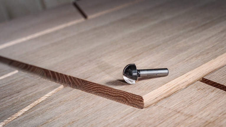 새로 잘라낸 홈이 있는 여러 겹의 목재 패널 위에 놓인 카바이드 라우터 비트입니다.