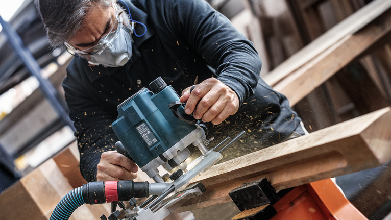 안전장비를 착용한 사람이 전동 라우터로 나무를 다듬고 있습니다.