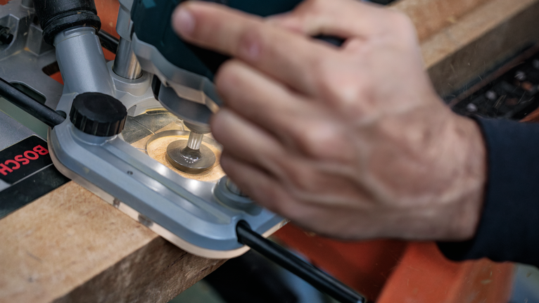 나무판의 가장자리 모양을 잡기 위해 라우터를 사용하는 사람.