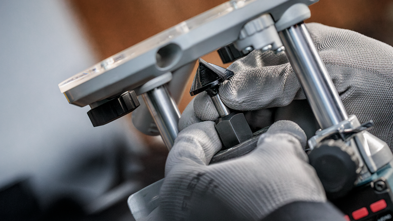 안전 장비를 착용한 사람이 전동 공구의 라우터 비트를 조정하고 있습니다.