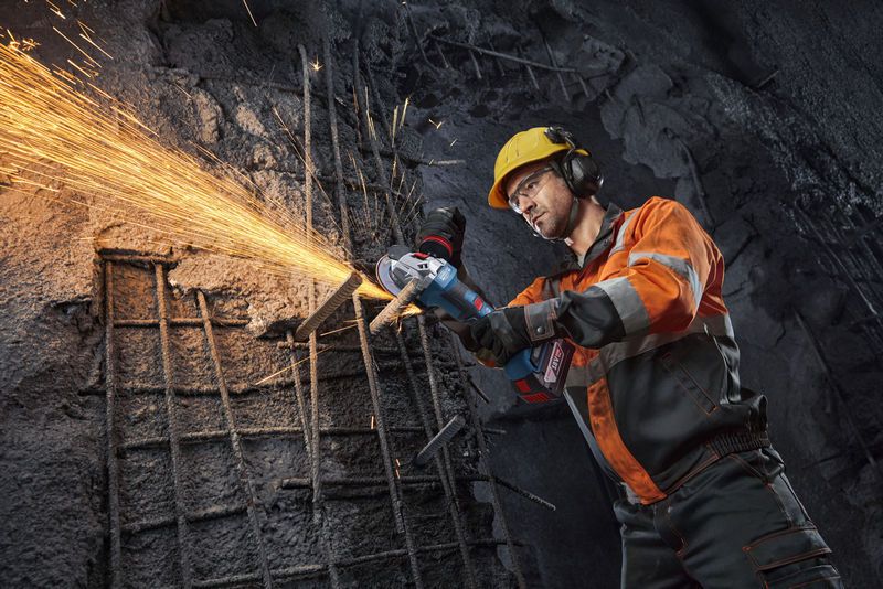 안전 장비를 착용한 사람이 앵글 그라인더로 철근을 절단하면서 불꽃이 튀고 있습니다.