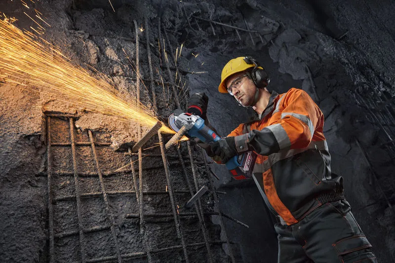 안전 장비를 착용한 사람이 앵글 그라인더로 철근을 절단하면서 불꽃이 튀고 있습니다.