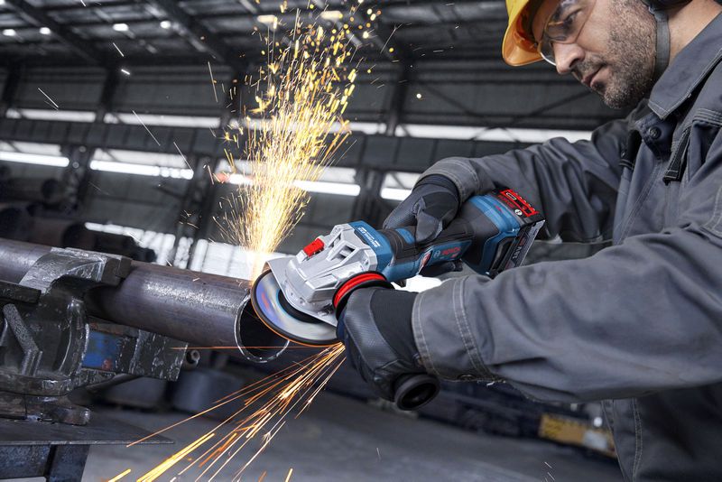 안전 장비를 착용한 사람이 앵글 그라인더로 금속 파이프를 갈아내면서 불꽃을 일으킨다.