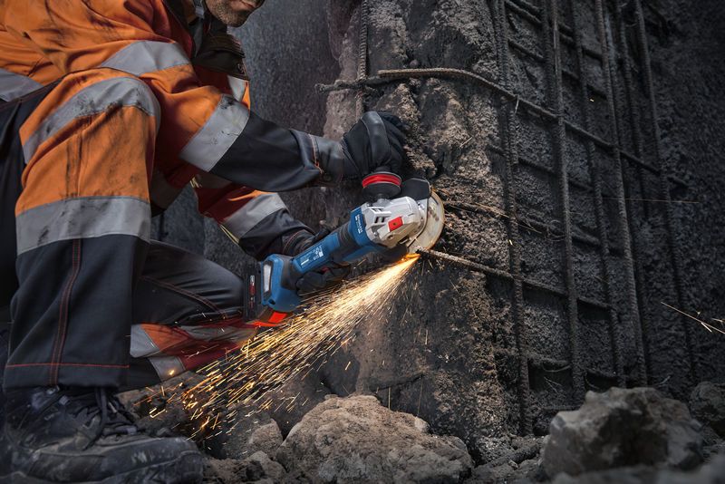 안전 장비를 착용한 사람이 앵글 그라인더로 콘크리트를 절단하면서 불꽃이 튀고 있다.