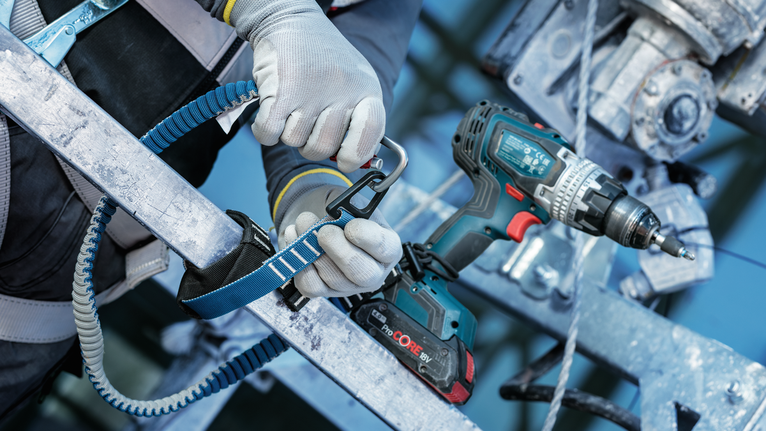 안전 장비를 착용한 사람이 금속 구조물의 무선 드릴 근처에 끈을 달고 있습니다.