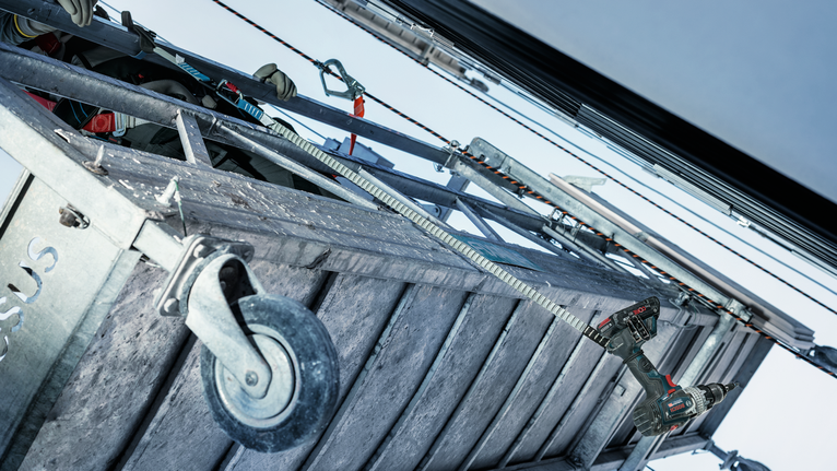 안전장비를 착용한 사람이 금속 구조물에 드릴을 사용하고 있습니다.