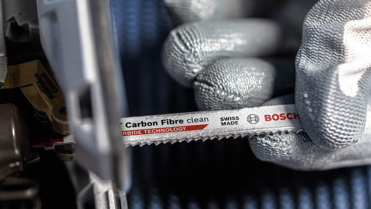 안전 장비를 착용한 사람이 전동 공구에 탄소 섬유 톱날을 설치하고 있습니다.