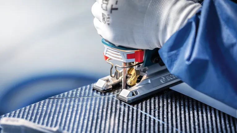 안전장비를 착용한 사람이 퍼즐 톱으로 무늬가 있는 패널을 자릅니다.