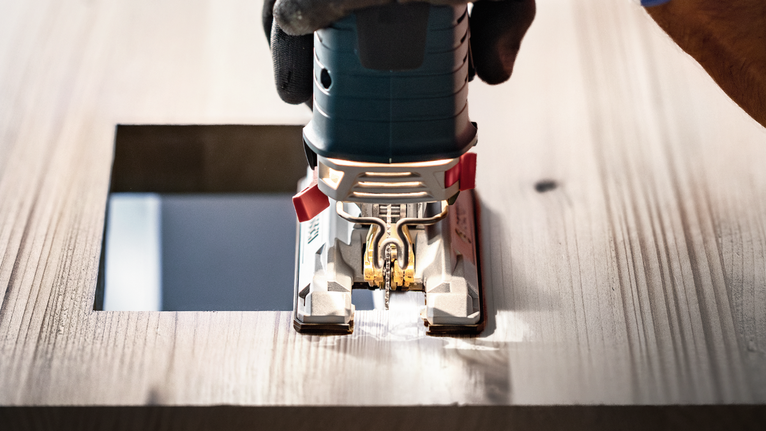 안전 장비를 착용한 사람이 톱을 사용해 나무에 정사각형 구멍을 자릅니다.