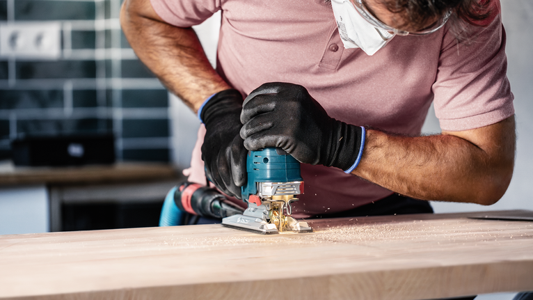 안전장비를 착용한 사람이 톱을 사용해 나무를 자릅니다.