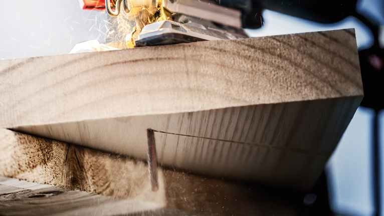 톱밥을 흩뿌리면서 두꺼운 나무 판자를 톱으로 자르는 모습.