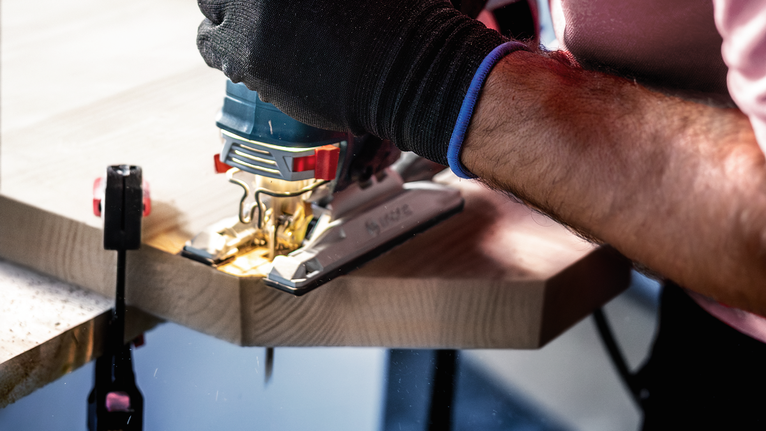 안전장비를 착용한 사람이 퍼즐 톱으로 나무 판자를 자릅니다.