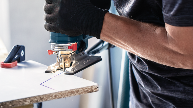 안전장비를 착용한 사람이 퍼즐 톱으로 표시된 판자를 자릅니다.