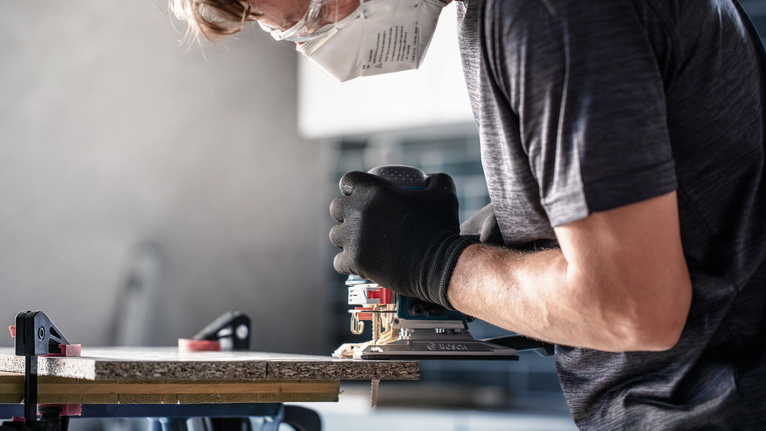 안전 장비를 착용한 사람이 전동 공구를 사용하여 나무를 자릅니다.