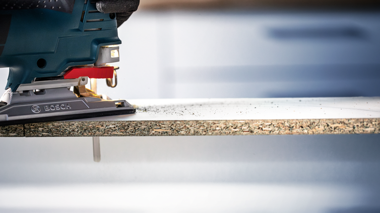 안전 장비를 착용한 사람이 퍼즐을 사용해 적층판을 자르고 있습니다.