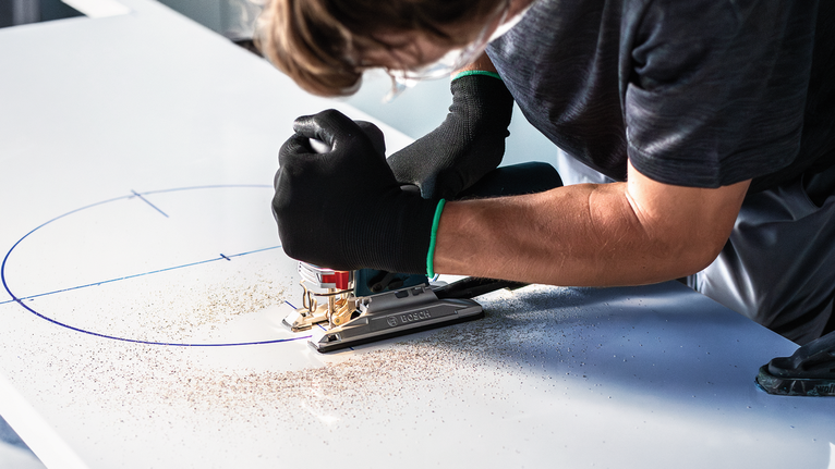 안전장비를 착용한 사람이 퍼즐을 사용해 표시된 보드에서 곡선을 자릅니다.