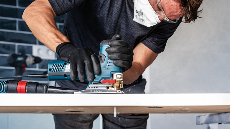 안전 장비를 착용한 사람이 전동 톱을 사용해 나무판을 자르고 있습니다.