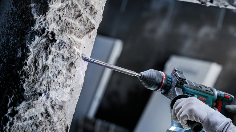 안전 장비를 착용한 사람이 전동 공구를 이용해 콘크리트에 구멍을 뚫고 있습니다.