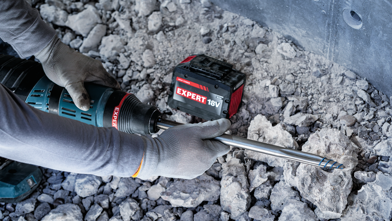 안전 장비를 착용한 사람이 바위가 많은 땅에서 무선 회전 망치를 작동하고 있습니다.