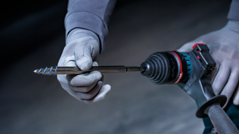 안전 장비를 착용한 사람이 전동 공구에 드릴 비트를 삽입하고 있습니다.