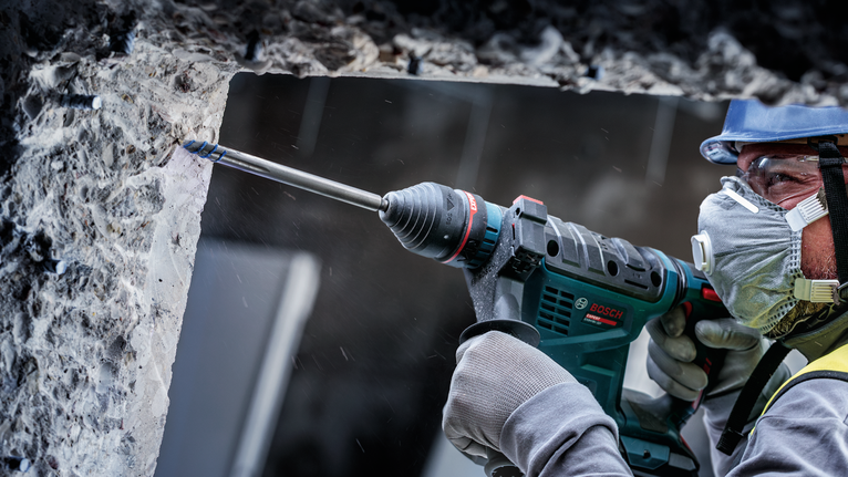 안전장비를 착용한 사람이 콘크리트 벽에 구멍을 뚫고 있습니다.