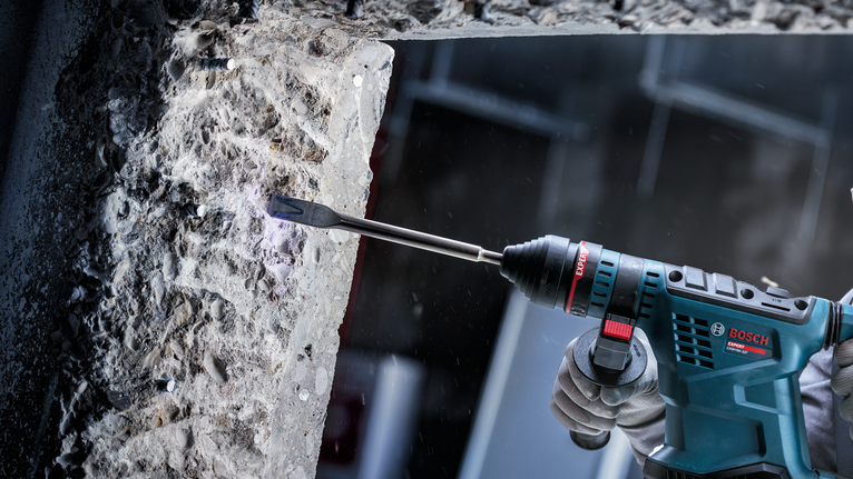 안전 장비를 착용한 사람이 전동 공구를 사용하여 콘크리트를 쪼개고 있습니다.