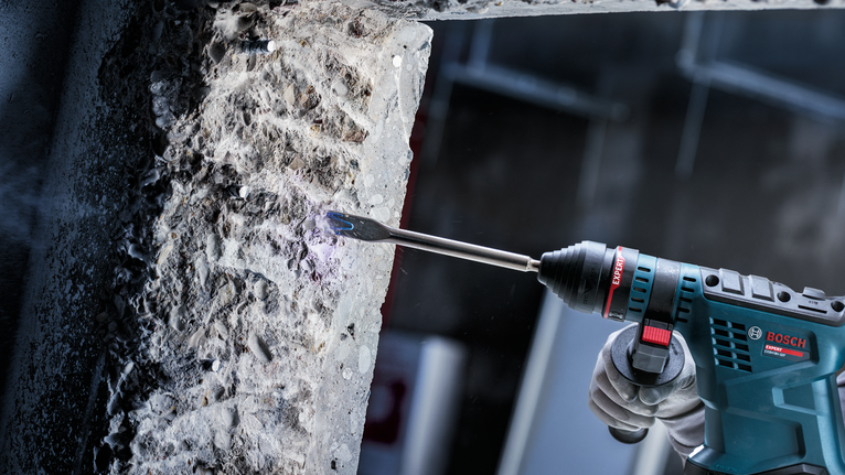 안전장비를 착용한 사람이 회전 망치로 콘크리트를 깎고 있습니다.