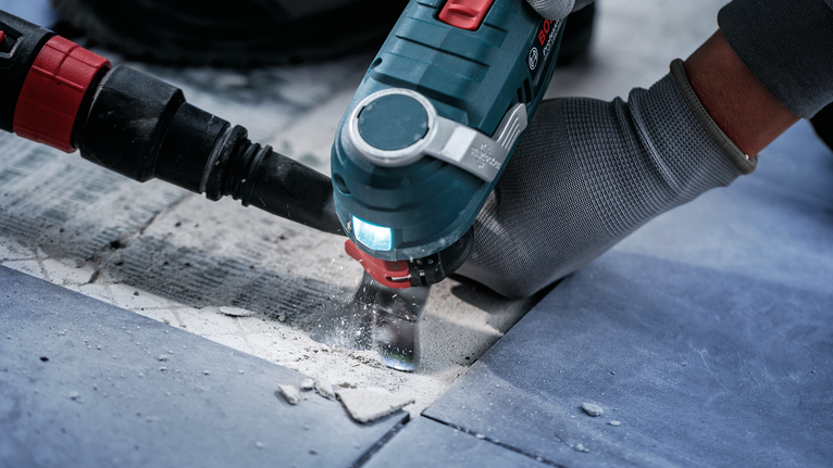 안전 장비를 착용한 사람이 전동 공구를 사용하여 타일을 자르고 있습니다.