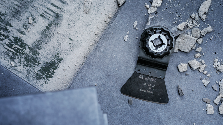 진동 공구의 날이 파편이 흩어진 타일 바닥 위에 놓여 있다.