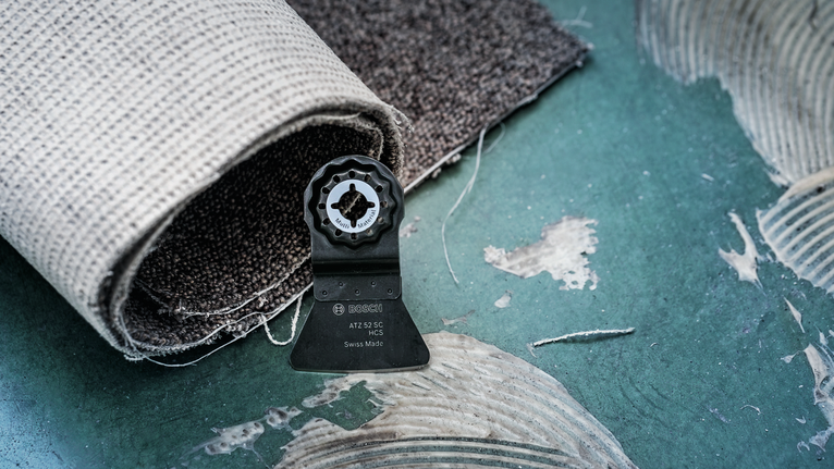 녹색 바닥 위에 놓인 진동 공구 날과 말아놓은 카펫.