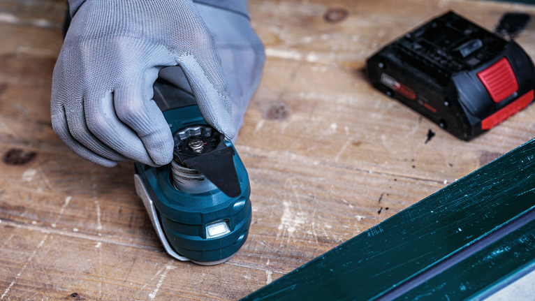 안전 장비를 착용한 사람이 작업대 위의 전동 공구에 날을 부착하고 있습니다.