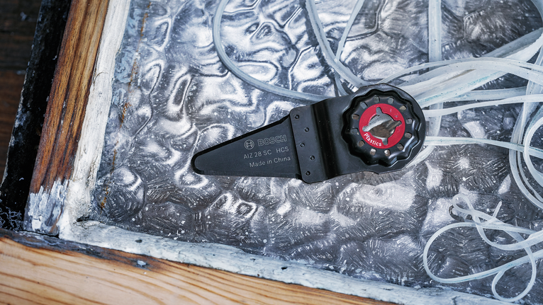 진동 공구 날 부착 장치는 나무 프레임 근처의 질감이 있는 금속판 위에 놓여 있습니다.