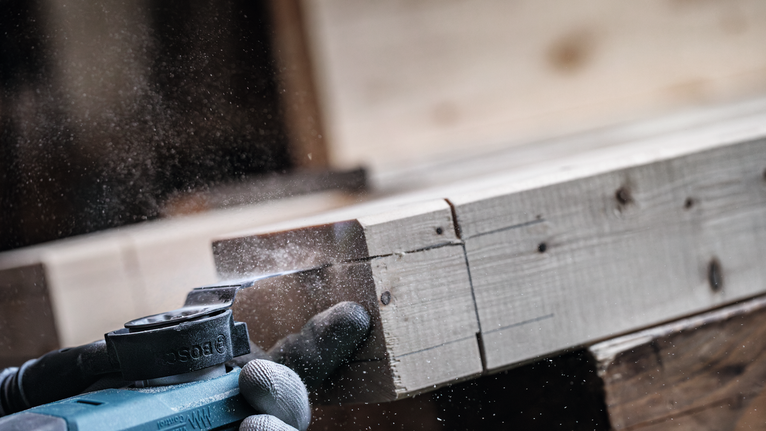 안전 장비를 착용한 사람이 전동 공구로 나무 판자를 사포질하고 있습니다.