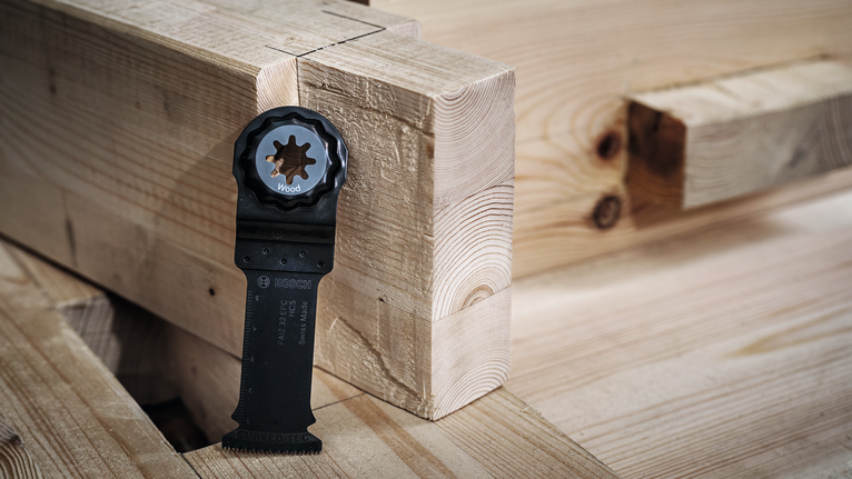 진동 공구의 날이 쌓아 놓은 나무 기둥 위에 똑바로 놓여 있다.