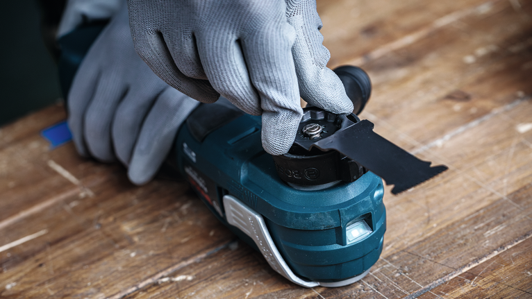 안전 장비를 착용한 사람이 전동 공구에 톱날을 장착하고 있습니다.