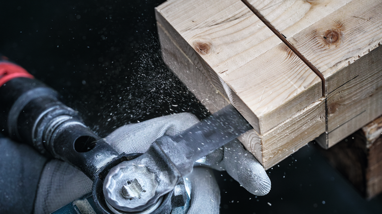 안전 장비를 착용한 사람이 전동톱으로 나무 기둥을 자르고 있습니다.