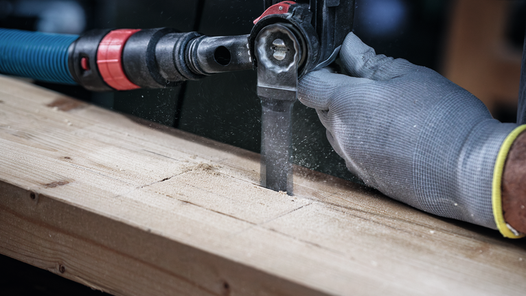 안전 장비를 착용한 사람이 왕복톱으로 나무 판자를 자르고 있습니다.