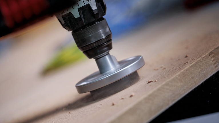 회전 공구를 사용하여 나무 판자의 가장자리를 샌딩하고 있습니다.