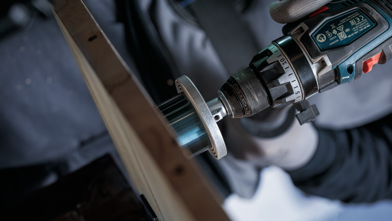 안전 장비를 착용한 사람이 전동 드릴의 구멍 뚫는 톱을 사용하여 나무에 구멍을 뚫고 있습니다.