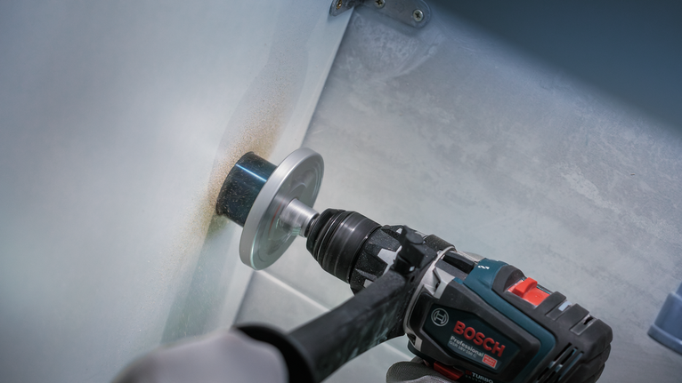 안전 장비를 착용한 사람이 홀쏘를 사용하여 금속에 구멍을 뚫고 있습니다.