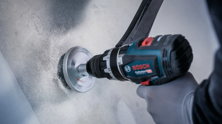 안전 장비를 착용한 사람이 금속 표면에 구멍을 뚫고 있다.