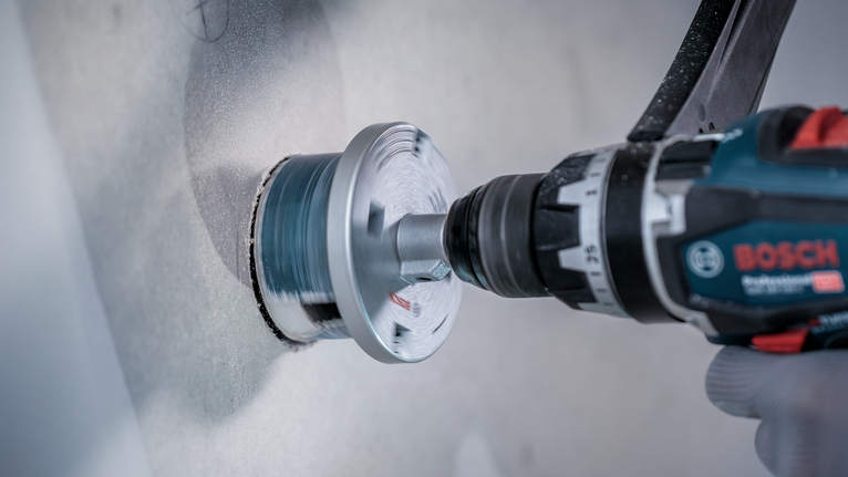 안전 장비를 착용한 사람이 벽에 원형 구멍을 뚫고 있다.